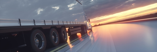 Commercial truck drives toward the sunset on a cloudy day