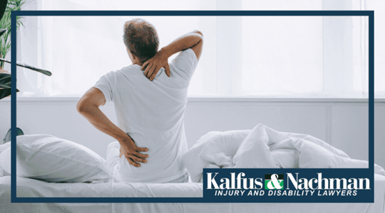 back view of man sitting on bed and suffering from back pain