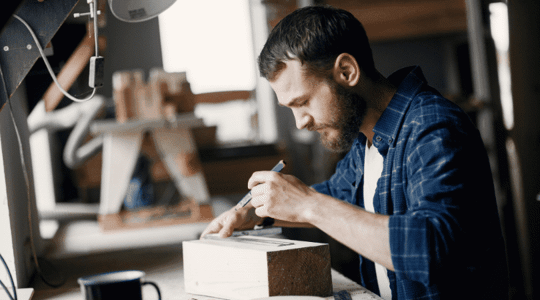 man measuring block of wood in his workshop