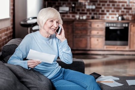 older woman sitting on couch while on the phone with a lawyer