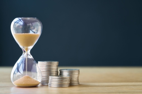 Sand hourglass and stack of coins to represent the time it takes to start earning benefits.