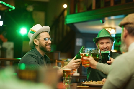 Group of happy men in traditional hats drinking beer and celebrating St. Patrick's Day in the pub