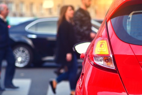 red car waiting at crosswalk as pedestrians cross the street
